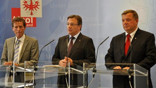 Drei Männer in Anzügen stehen an einem Rednerpult vor einem Hintergrund mit dem Tiroler Adler.