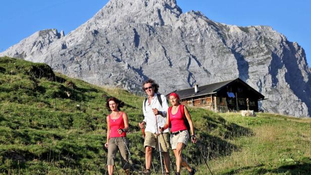 Drei Wanderer vor einer Berghütte und einem großen Bergmassiv.