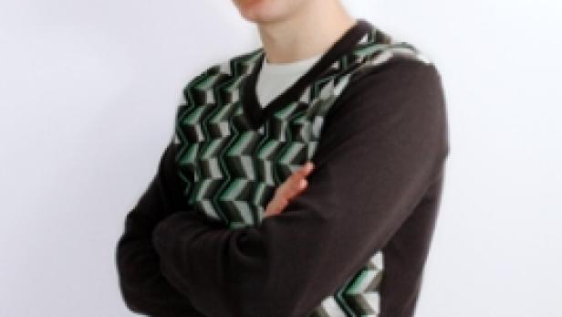 Ein junger Mann mit verschränkten Armen trägt einen gemusterten Pullover.
