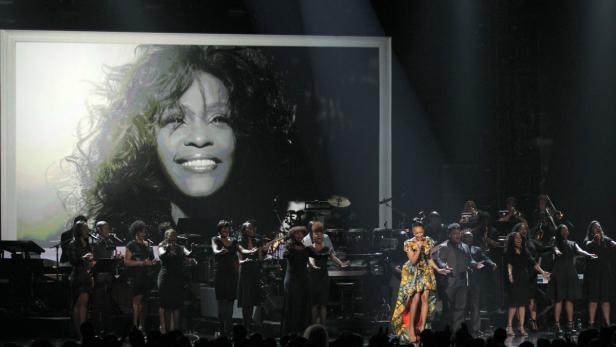 Eine Sängerin tritt vor einem großen Bild von Whitney Houston mit einem Chor und einer Band auf.