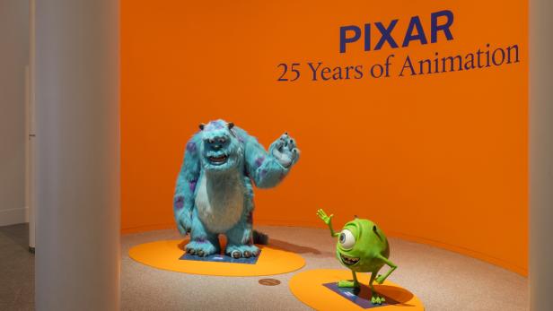Sully und Mike Glotzkowski, Figuren aus „Die Monster AG“, stehen vor einer Wand mit der Aufschrift „Pixar: 25 Years of Animation“.