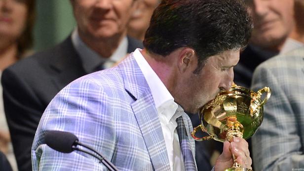 Ein Mann im karierten Sakko küsst einen goldenen Pokal.