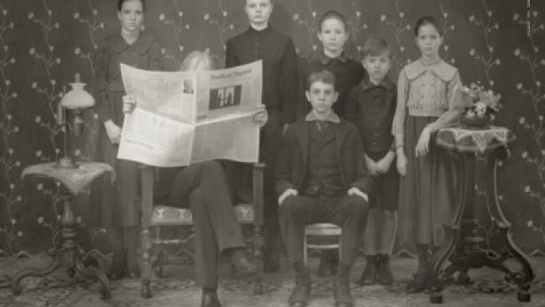 Ein formelles Familienporträt in Sepia mit einem Mann, der eine Zeitung liest.