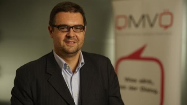 Ein Mann mit Brille und Anzug steht vor einem OMVÖ-Banner.