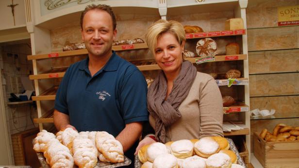 Ein Bäcker und eine Bäckerin präsentieren Gebäck in einer Bäckerei.