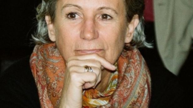 Eine Frau mit grauem Haar und einem gemusterten Schal denkt nach.