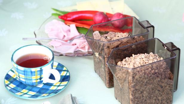 Ein Frühstückstisch mit Müsli, Aufschnitt, Gemüse und einer Tasse Tee.