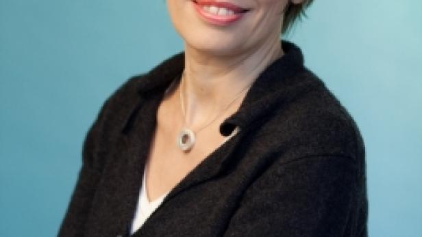 Eine Frau mit kurzem braunem Haar lächelt mit verschränkten Armen in die Kamera.