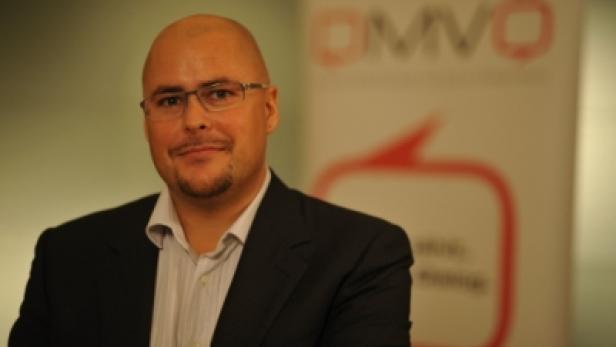 Ein Mann mit Brille und Anzug posiert vor einem OMV-Banner.