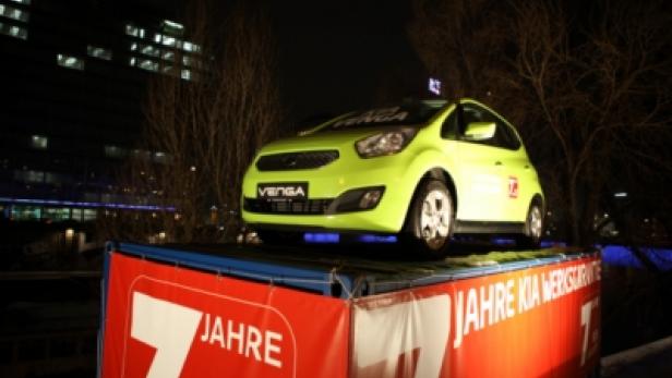 Ein hellgrüner Kia Venga steht auf einem Podest mit der Aufschrift „7 Jahre Kia Werksgarantie“.
