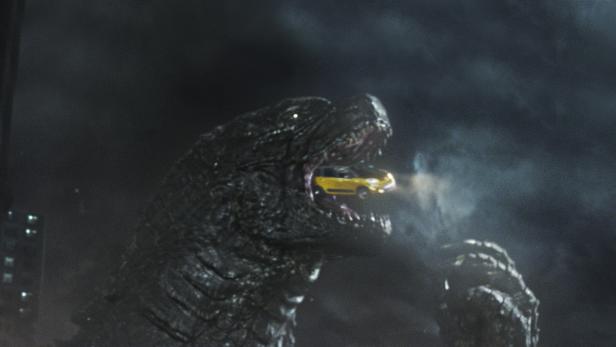Godzilla hat ein gelbes Taxi im Maul.