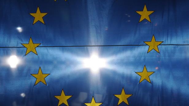 Die Europaflagge mit gelben Sternen vor einem hellen Licht.