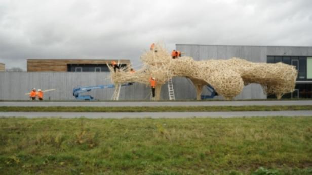 Mehrere Arbeiter errichten eine große Holzskulptur im Freien.