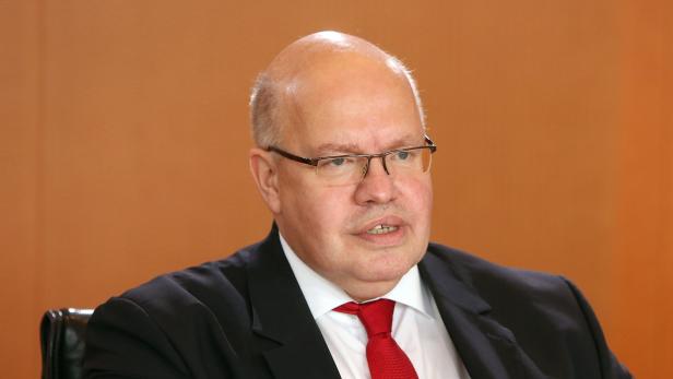 Ein Mann mit Brille und roter Krawatte vor einem orangefarbenen Hintergrund.