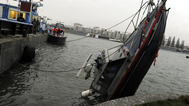 Ein gekentertes Boot namens „Fischa“ liegt im Wasser, während andere Boote in der Nähe sind.