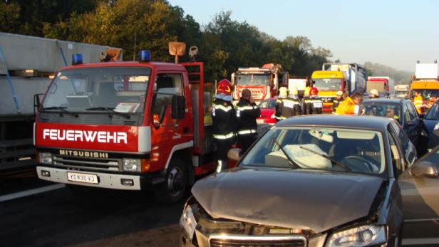 Ein beschädigter Audi steht neben einem Feuerwehrfahrzeug auf einer Autobahn.