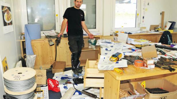 Ein Mann steht in einem unordentlichen Büro mit Werkzeugen und Materialien.