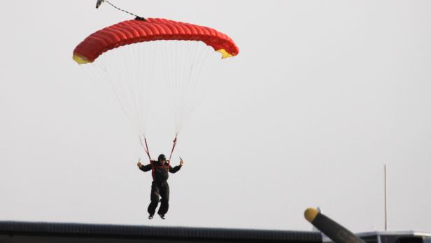 Ein Fallschirmspringer mit rotem Fallschirm landet.