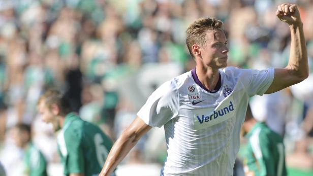 Ein Fußballspieler jubelt mit erhobenem Arm vor einer Zuschauermenge.