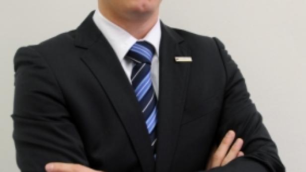 Ein Mann im Anzug mit verschränkten Armen vor einem hellen Hintergrund.