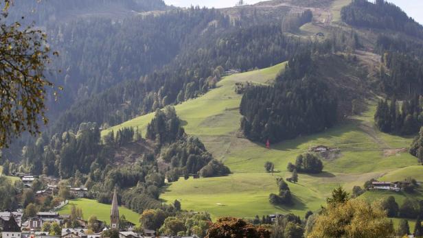 Blick auf ein Dorf in einem grünen Tal mit bewaldeten Hügeln im Hintergrund.