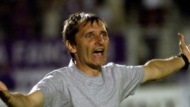 Ein Mann mit grauem T-Shirt gestikuliert auf einem Fußballfeld.