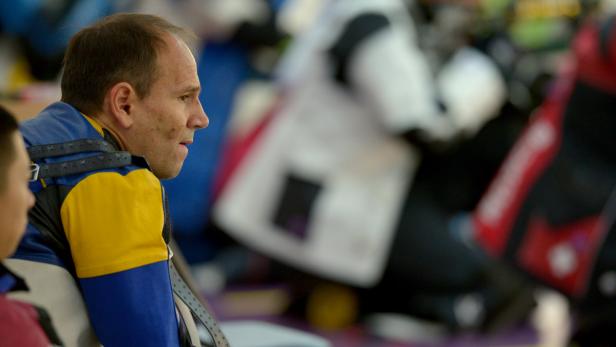 Ein Mann in Sportkleidung sitzt und schaut nach rechts.