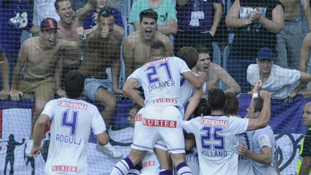 Fußballspieler umarmen sich auf dem Spielfeld, während Fans im Hintergrund jubeln.
