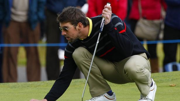 Ein Mann mit Sonnenbrille kauert auf einem Golfplatz und zielt mit einem Putter.