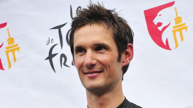 Ein Porträt des Radrennfahrers Bradley Wiggins vor einem Tour de France-Hintergrund.