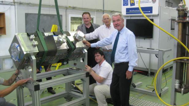 Eine Gruppe von Personen hantiert mit einem großen, metallischen Gerät in einer Forschungseinrichtung.