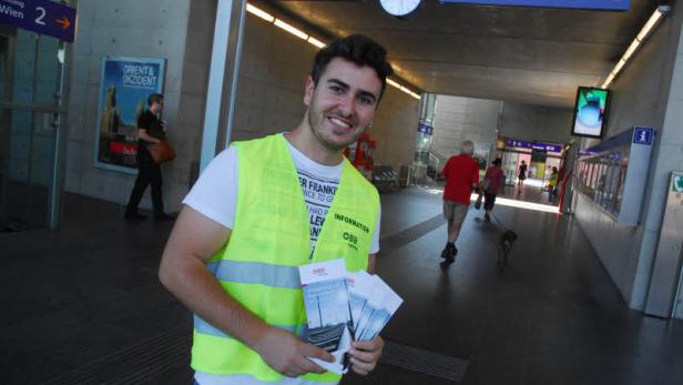 Ein ÖBB-Mitarbeiter in einer Bahnhofshalle mit Flyern in der Hand.