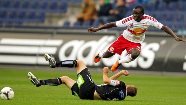 Ein Fußballspieler springt über einen am Boden liegenden Gegenspieler.