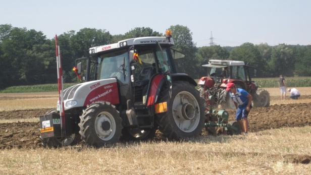 Zwei Steyr-Traktoren pflügen ein Feld, während Personen zusehen.