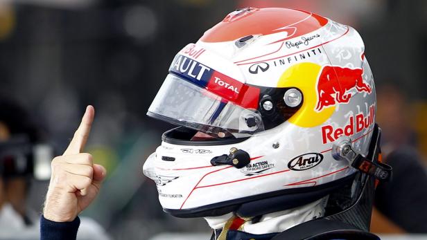 Ein Rennfahrer mit Helm zeigt mit dem Finger nach oben.