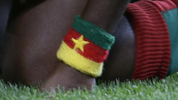 Ein Arm mit einer Strickmanschette in den Farben der kamerunischen Flagge.