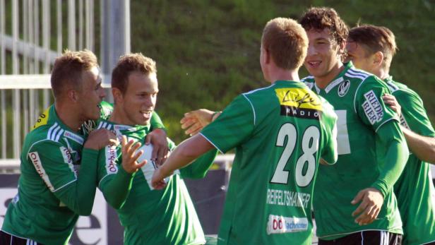 Mehrere Fußballspieler in grünen Trikots feiern gemeinsam auf dem Spielfeld.