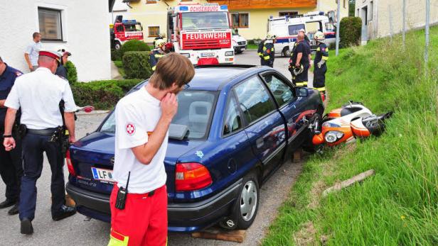 Ein blauer Opel Astra und ein Motorroller sind in einen Unfall verwickelt; Feuerwehr und Rettungsdienst sind vor Ort.