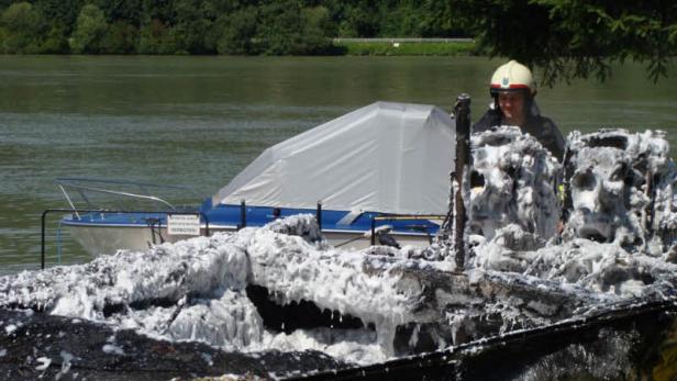 Ein Feuerwehrmann untersucht ein ausgebranntes Boot auf einem Fluss.
