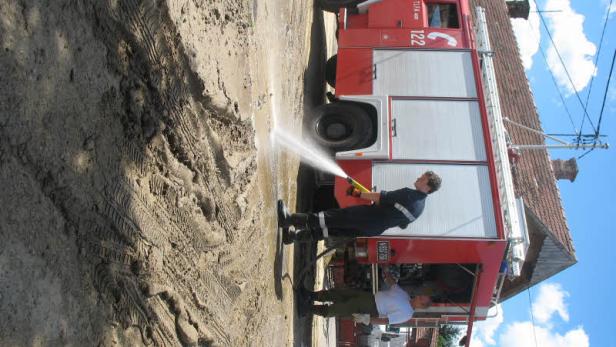 Ein Feuerwehrmann spritzt mit einem Schlauch Wasser auf eine schlammige Straße.