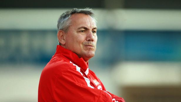 Ein Mann in roter Jacke mit verschränkten Armen blickt nach rechts.