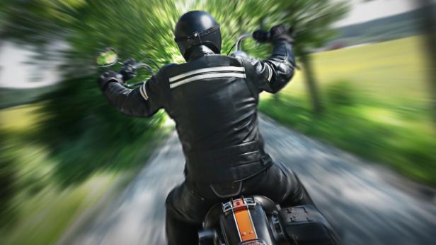 Ein Motorradfahrer in Lederkleidung fährt auf einer Landstraße.