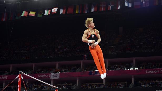 Ein Turner in oranger Hose springt am Reck bei den Olympischen Spielen in London 2012.