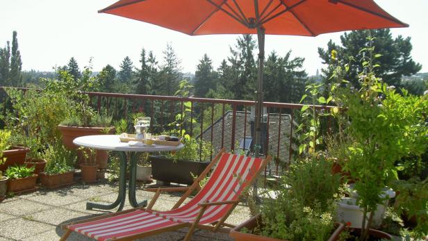 Ein sonniger Balkon mit Liegestuhl, Tisch und vielen Pflanzen.