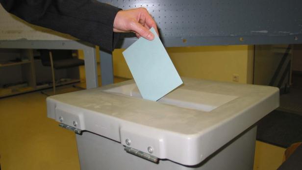 Eine Hand wirft einen Stimmzettel in eine Wahlurne.