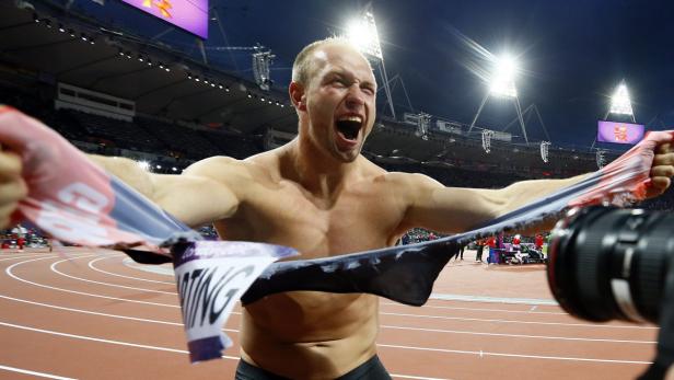Ein muskulöser Mann zerreißt sein Trikot auf einer Leichtathletikbahn.