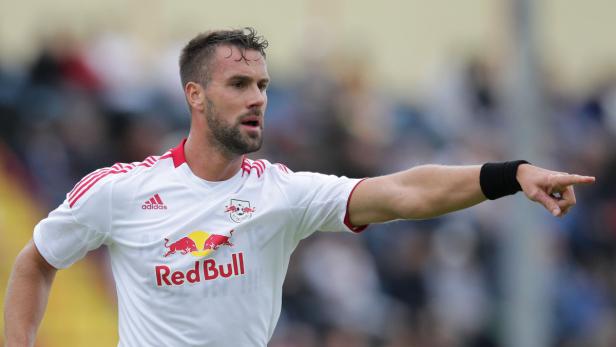 Ein Fußballspieler in einem weißen Trikot von Red Bull zeigt mit dem Finger nach rechts.