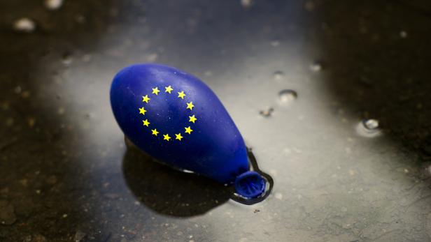 Ein blauer, geplatzter Ballon mit dem Aufdruck der Europaflagge liegt in einer Pfütze.