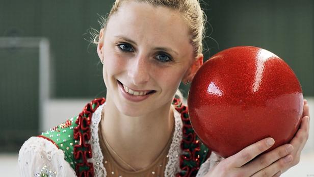 Eine rhythmische Sportgymnastin hält einen roten Ball.