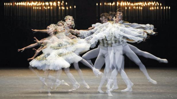 Mehrere Tänzer und Tänzerinnen in Kostümen führen eine Ballettaufführung auf einer Bühne auf.